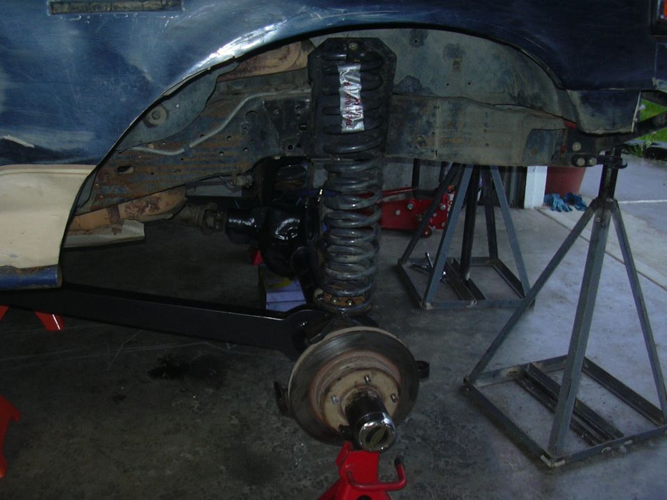 Blue truck front suspension on jack stands showing coilover, radius arm and bare brake rotor