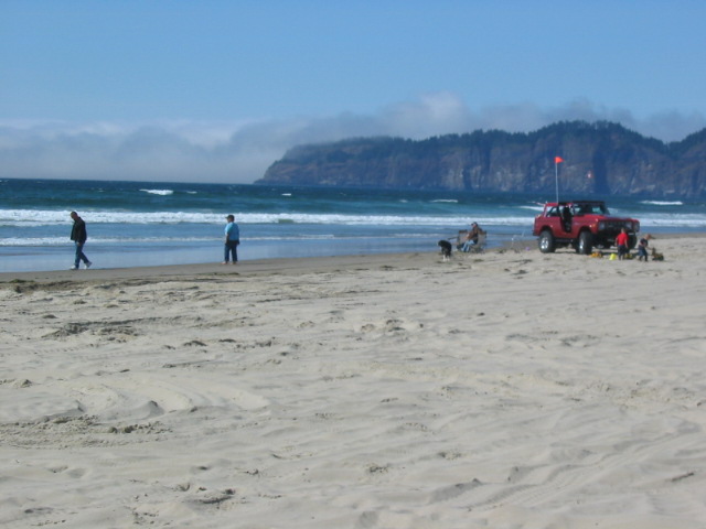 Red SUV parked on a beach near the ocean surf with people nearby
