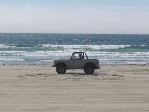 1995 Ford Bronco - A classic Ford Bronco is driven along the shore, kicking up sand near the ocean waves.