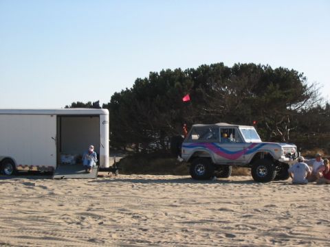 1995 Ford Bronco - A lifted Ford Bronco sits on the sand next to a trailer, with people gathered nearby.