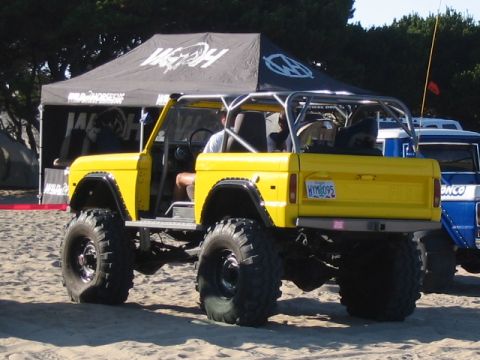 1995 Ford Bronco - A lifted yellow Bronco with a roll cage sits on a sandy beach next to a blue Bronco.