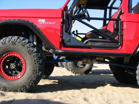 1995 Ford Bronco - A red 1995 Ford Bronco is shown with its door open, revealing a roll cage and off-road tires.