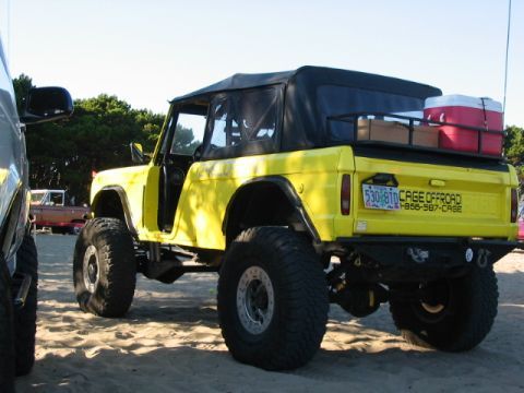 1995 Ford Bronco - Yellow lifted Ford Bronco with soft top parked on sand, with a cooler on the roof rack.