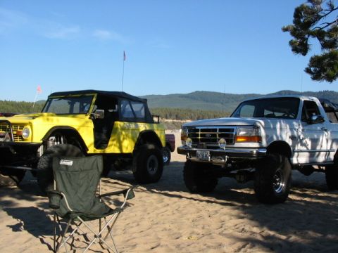 1995 Ford Bronco - A white Ford F-150 pickup truck is parked on a sandy beach next to a yellow off-road vehicle.