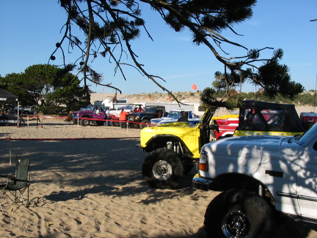 White and yellow lifted trucks on big tires parked on sand near dunes