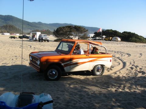 1995 Ford Bronco - Ford Bronco driving on sand dunes with other vehicles and campers in the background.
