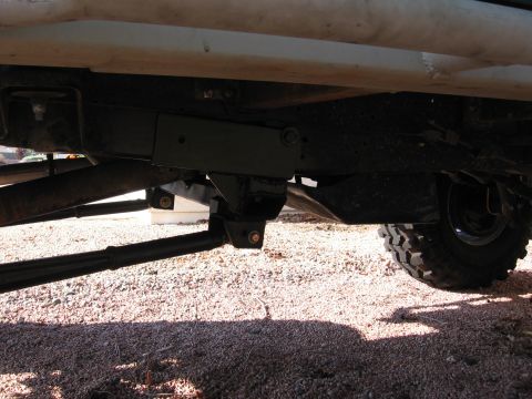 1990 Ford Bronco - The underside of a vehicle shows its suspension system and a tire on a gravel surface.