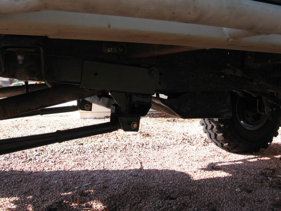 Underbody view of a lifted white truck showing black frame, crossmember and off-road tire