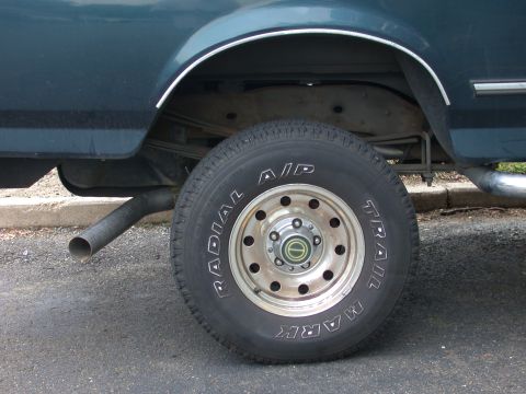 1995 Ford Bronco - Rear view of a dark green SUV showing the exhaust pipe and a Radial A/P Trail Mark tire.