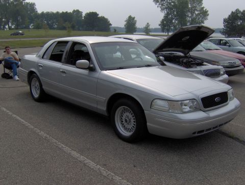 2002 Ford Crown Victoria - A silver sedan is parked in a lot with its hood open, alongside other vehicles.