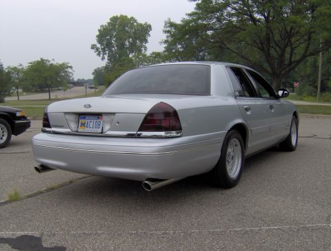 2002 Ford Crown Victoria - A silver 2002 Ford Crown Victoria sedan is viewed from the rear, parked on asphalt with trees in the background.