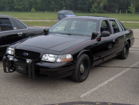 2002 Ford Crown Victoria - A black 2002 Ford Crown Victoria, likely a police interceptor, is parked next to another dark vehicle.