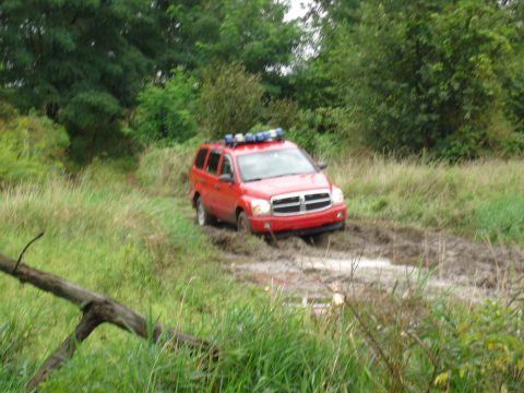 1979 Ford Bronco - Red Dodge Durango with light bar navigates a muddy off-road path.
