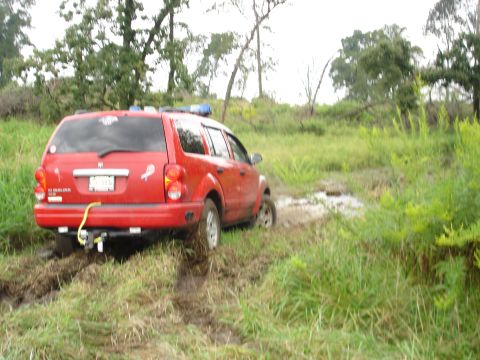 1979 Ford Bronco - A red SUV is stuck in the mud, with its rear end facing the camera.