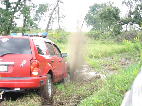 1979 Ford Bronco - Red SUV with blue lights navigates a muddy off-road trail.