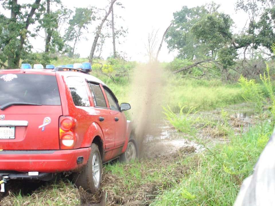 Red SUV with blue lights driving through mud, rear view