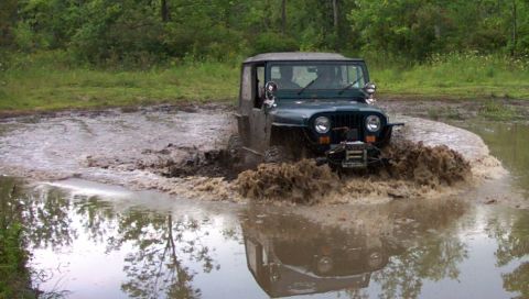 1979 Ford Bronco - Off-road Jeep Wrangler navigates a deep mud puddle, creating a large splash.