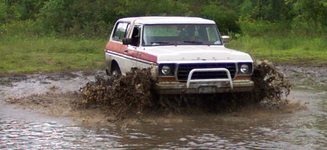 White and red Ford Bronco driving through mud, front bull bar visible