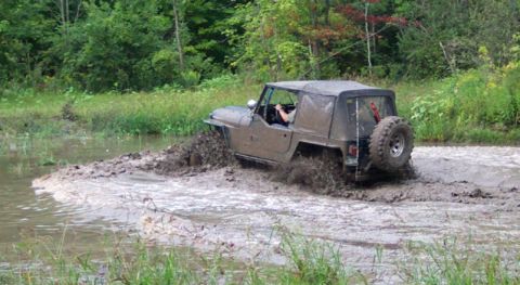 1979 Ford Bronco - A Jeep CJ-7 navigates a muddy water obstacle, kicking up a large spray.