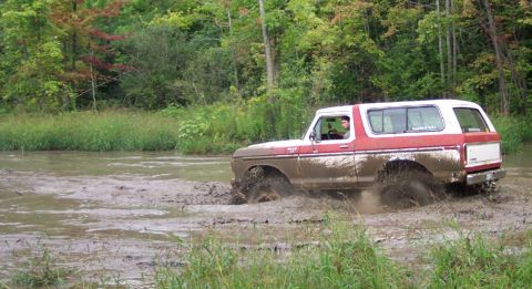 1979 Ford Bronco - A driver navigates a muddy terrain in a classic Ford Bronco, splashing through the mire.
