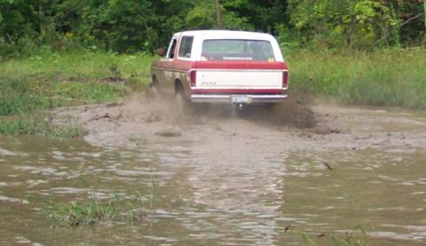 1979 Ford Bronco - A red and white Ford Bronco navigates a muddy obstacle course.