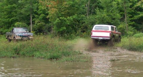 1979 Ford Bronco - A 1979 Ford Bronco kicks up mud as it navigates off-road, with another truck visible in the background.
