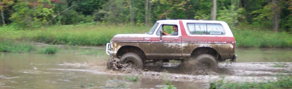Muddy 1978 Ford Bronco driving through water and splashing mud