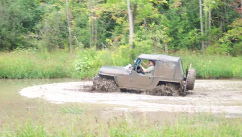 1979 Ford Bronco - A Jeep CJ-8 Scrambler navigates a muddy terrain, kicking up dirt and water.