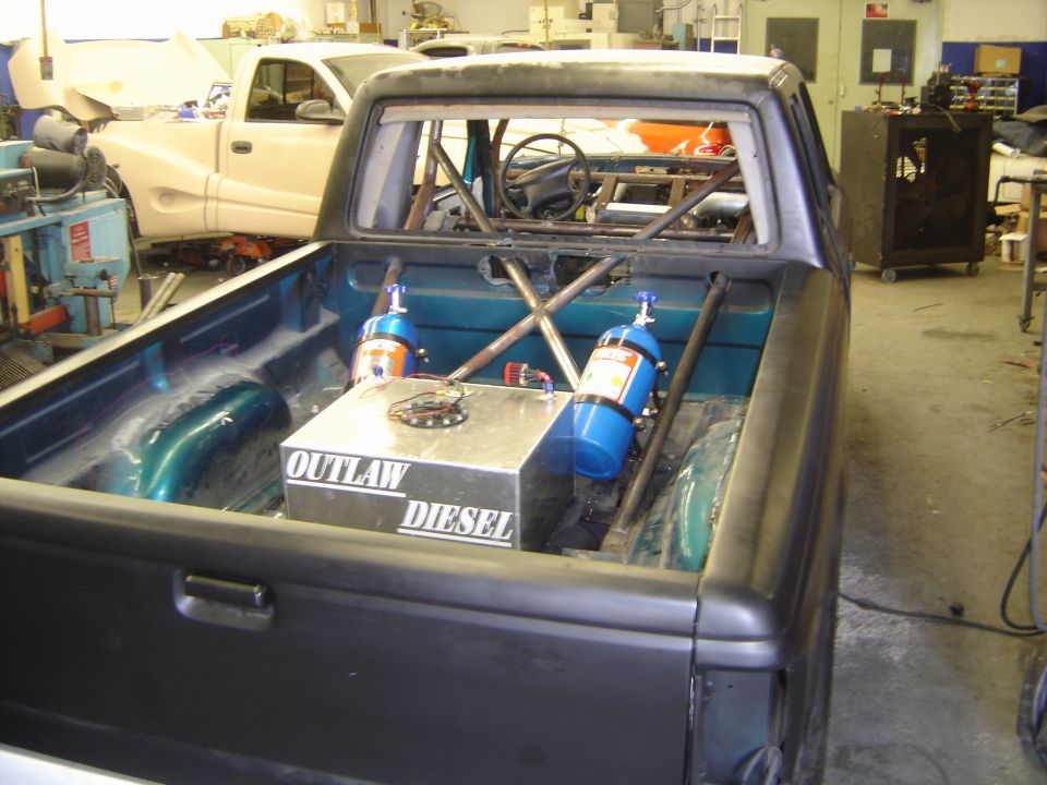 Pickup bed with roll cage, aluminum fuel cell and two blue nitrous bottles in a shop.