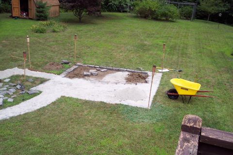 2001 Ford Crown Victoria - A yellow wheelbarrow sits beside a patio area under construction, with tiki torches marking the perimeter.