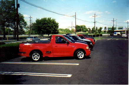 1989 Ford Mustang - A red 1999 Ford F-150 Lightning pickup truck is seen parked in a lot with other vehicles.