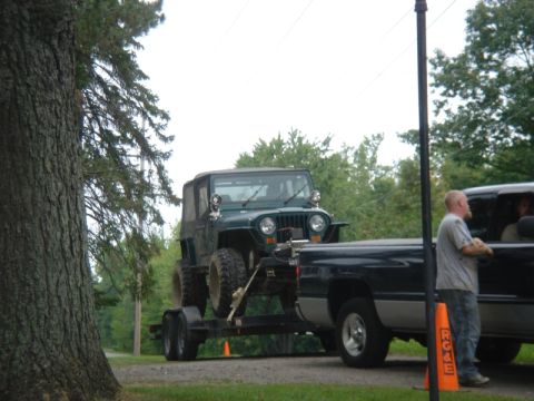 1979 Ford F-250 - A Jeep Wrangler is loaded onto a trailer and towed by a pickup truck on a rural road.