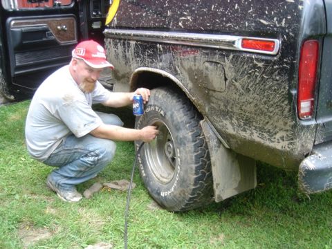 1979 Ford F-250 - A man is seen airing up the tire of a muddy truck, likely after off-roading.