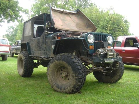1979 Ford F-250 - A heavily modified Jeep Wrangler sits on a grassy field, its hood propped open, revealing the engine bay.