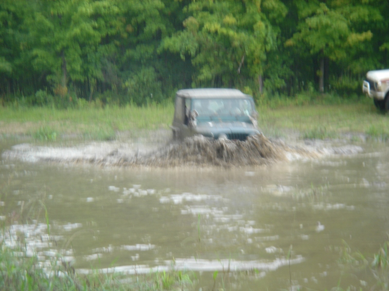 Dark SUV splashing through mud puddle, another vehicle in background