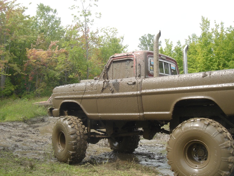 Muddy pickup truck with tall exhaust pipes, stuck in a muddy field with trees in the background