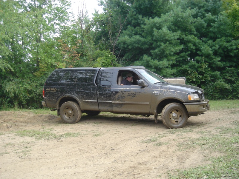 Black pickup truck with camper shell, side view. Muddy