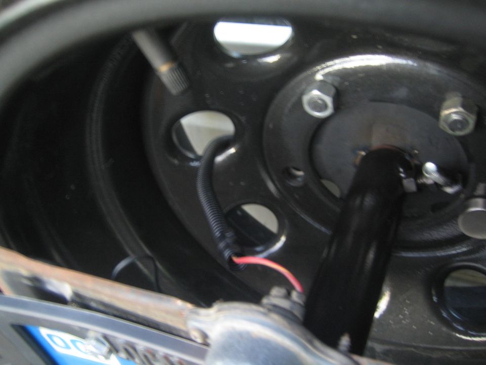 Close-up of a black wheel hub with visible lug nuts and wiring, showing part of the suspension