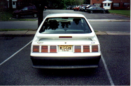 1989 Ford Mustang - The rear of a white 1987 Ford Mustang is visible, parked in a lot with other vehicles.