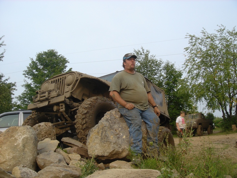 Muddy off-road vehicle with large tires and a man sitting on a rock