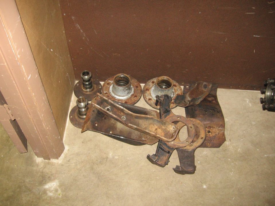 Pile of rusty truck axle components including hubs and spindles on concrete floor