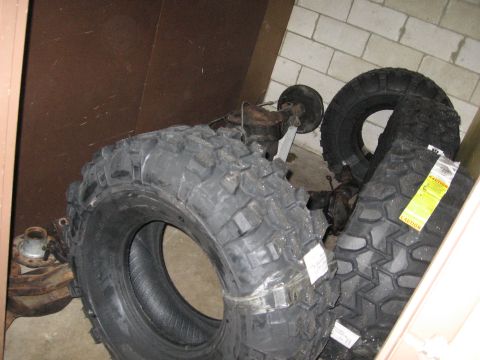 1974 Ford F-100 - Vehicle axles and large off-road tires are stored together, suggesting parts for a vehicle modification.