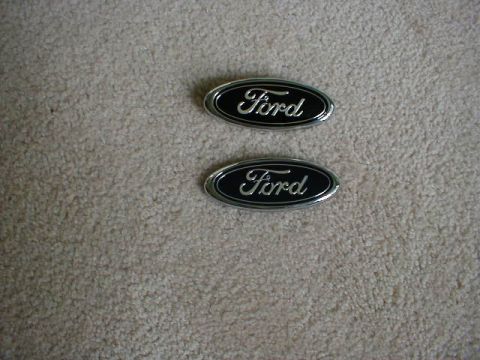 2002 Ford Crown Victoria - Two Ford oval emblems are shown on a carpeted surface.