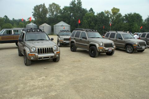 2006 Jeep Liberty - Several tan 2006 Jeep Liberty SUVs are parked in a gravel lot with silos and trees in the background.