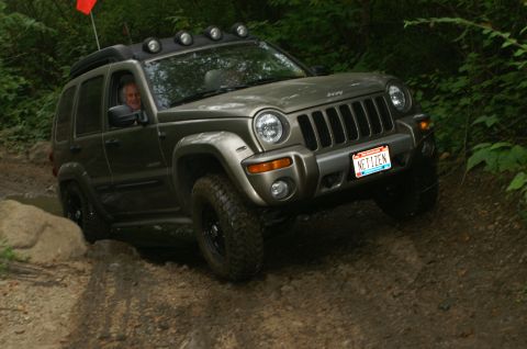 2006 Jeep Liberty - A 2006 Jeep Liberty navigates a challenging off-road course, kicking up dirt and mud.