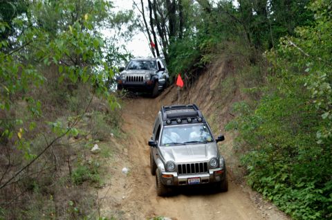2006 Jeep Liberty - Two Jeep Libertys navigate a steep, wooded off-road trail, kicking up dust as they descend.