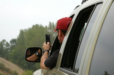 2006 Jeep Liberty - Man using a flip phone to take a photo while leaning out of a car window.