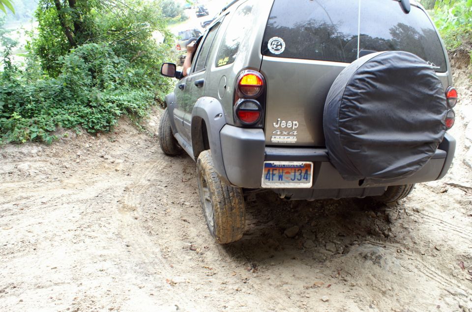 2006 Jeep Liberty with spare tire on back driving on a dirt trail; another vehicle visible in background