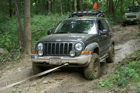 2006 Jeep Liberty - Two Jeeps navigate a challenging, muddy off-road course surrounded by dense forest.