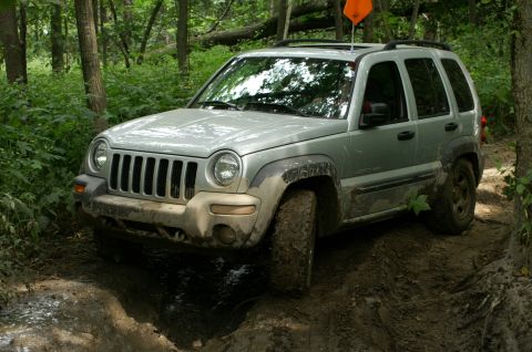 2006 Jeep Liberty - Silver Jeep Liberty navigates a muddy off-road path with an orange flag on its roof.